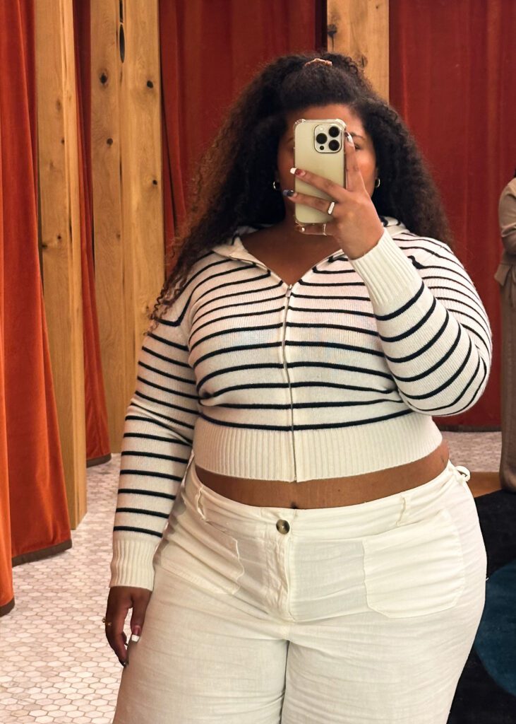 Close-up of a plus-size woman wearing Aritzia's striped cashmere zip-up hoodie with white jeans.