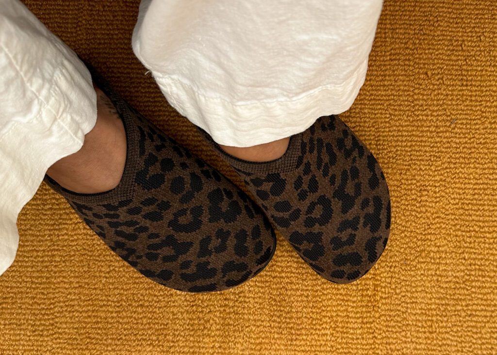 Overhead view of a plus-size woman's feet wearing Rothy's Casual Clog in ReVelvet Cheetah with white wide-leg pants.